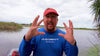 A person in a blue shirt with his hands up with a lake behind